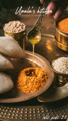 Spoon drizzling oil over Idli podi on a wooden plate withUpala's Kitchen branding.