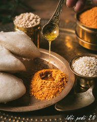 Idli with chutney and spices on a metal tray, with a hand holding a spoon.